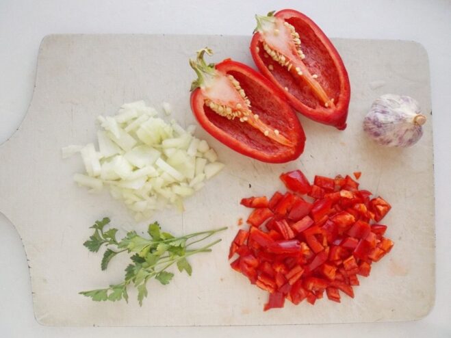 Chopping Vegetables for the Ratatouille Sauce Finely chopped onion, diced red bell pepper, and fresh herbs on a cutting board.