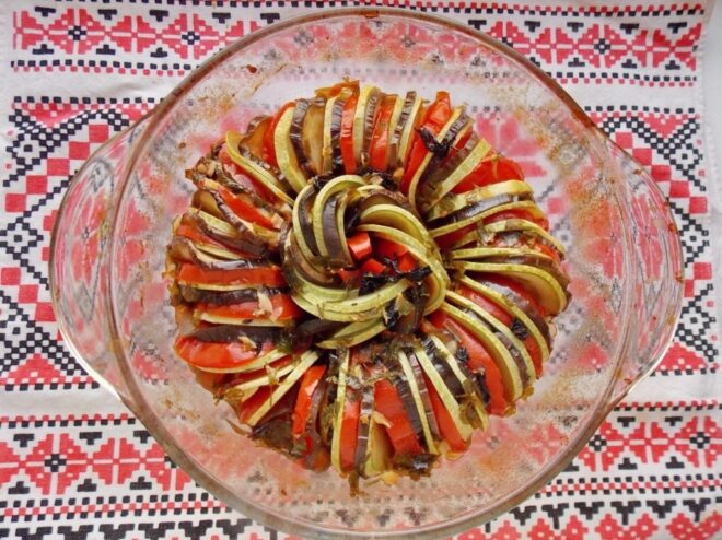 A serving of freshly baked Ratatouille on a white plate, garnished with herbs.