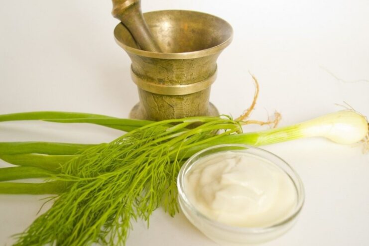 Making the dill sauce by grinding fresh dill with salt in a mortar. A mortar and pestle being used to grind fresh dill and salt to make a sauce.