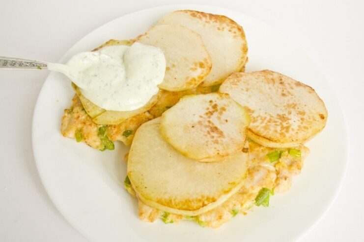 Serving the chicken and kohlrabi dish with a generous drizzle of creamy dill sauce. A hand pouring a creamy green dill sauce over chicken cutlets topped with kohlrabi.