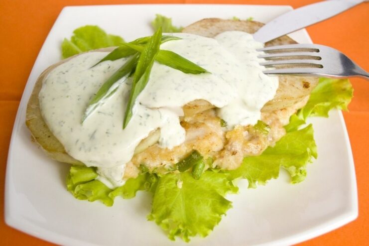 A plate with minced chicken cutlets topped with kohlrabi slices and a creamy green dill sauce.