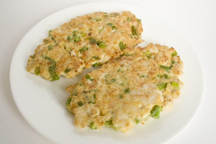 Golden-brown chicken cutlets frying in a pan. Two large chicken cutlets being fried to a golden-brown color in a black frying pan.
