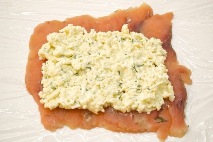 The creamy cheese filling being spread evenly over the layer of sliced cured salmon.