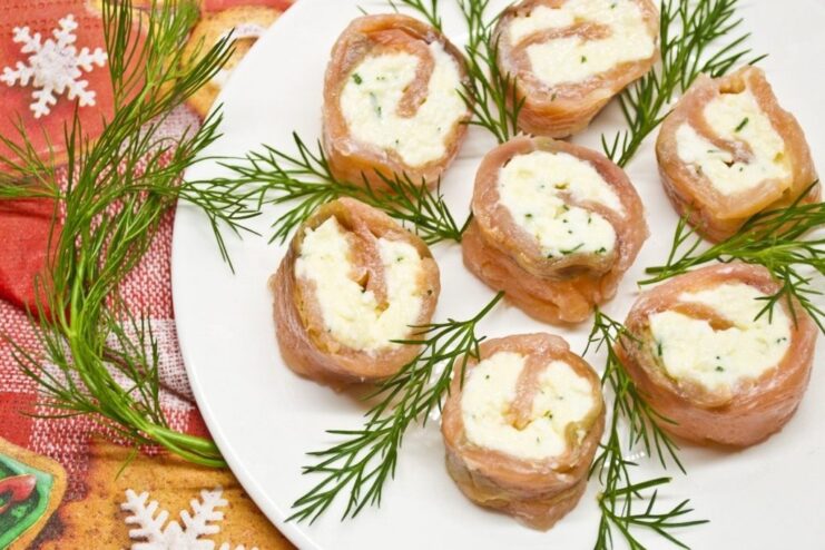 A plate of sliced homemade cured red fish rolls with a creamy cheese filling, garnished with fresh herbs.