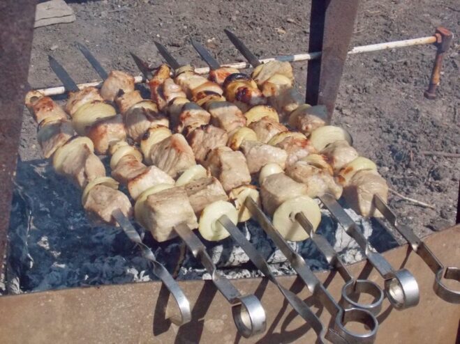The Key to Juicy Shashlik: Turn Skewers Regularly A hand turning shashlik skewers on a mangal to ensure they cook evenly.