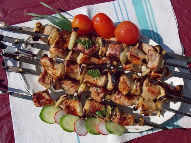 A plate of perfectly grilled shashlik skewers, garnished with herbs and ready to be served.