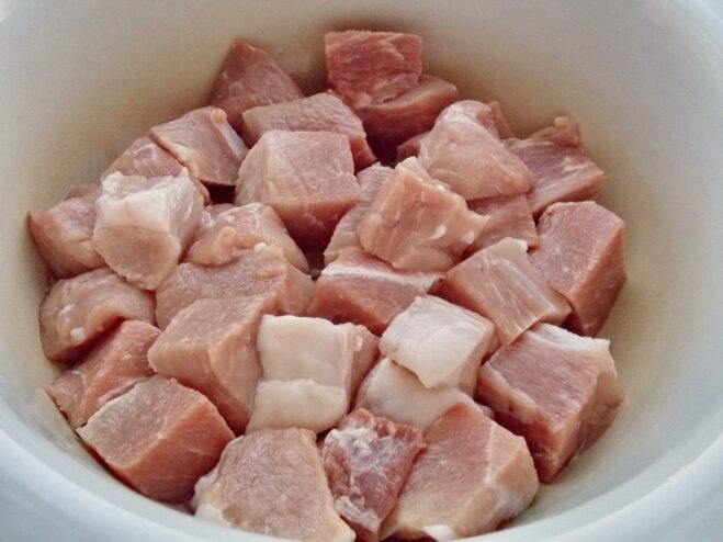 Cutting Meat for Shashlik - The First Step to Perfection Cubes of raw meat in an enamel bowl, cut into even pieces for shashlik.