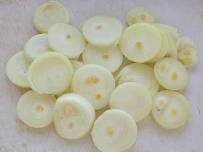 Preparing Onions for the Shashlik Marinade A hand slicing a white onion into thin rings on a wooden cutting board.