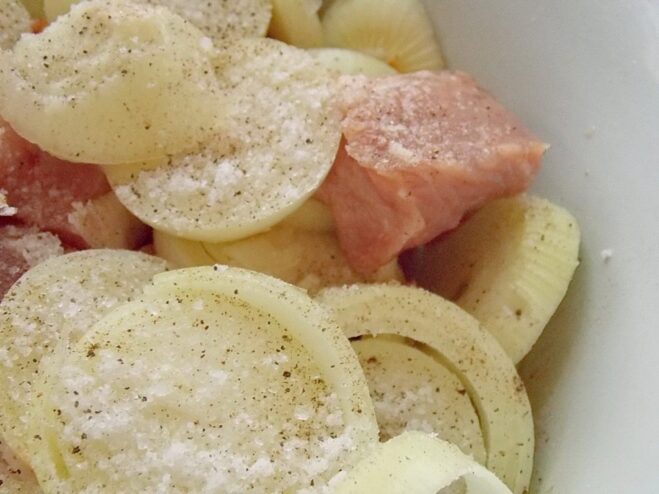 Combining Ingredients for the Perfect Shashlik Marinade A bowl with cubed meat, onion rings, and spices being mixed together by hand.
