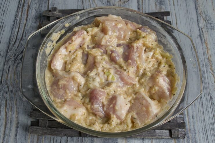 Thoroughly coating the pork pieces with marinade before refrigerating. Pork chunks being mixed by hand with the marinade in a large bowl.