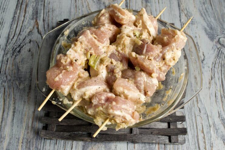 Threading the marinated pork chunks tightly onto bamboo skewers. Marinated pork pieces being threaded onto a bamboo skewer.
