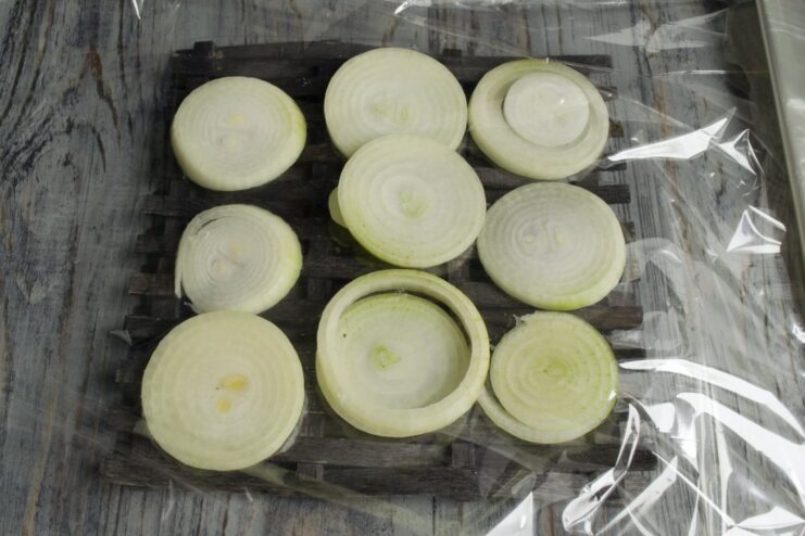 Creating a bed of onion rings inside the baking sleeve for extra flavor. A layer of large onion rings placed inside a clear baking sleeve.