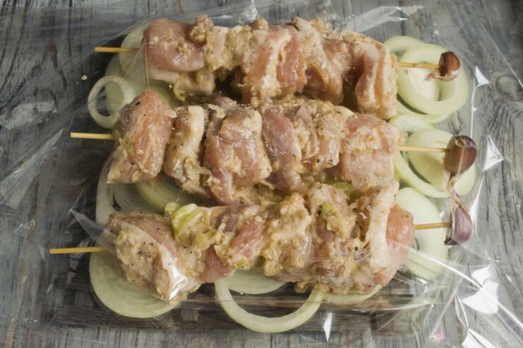 Arranging the pork skewers over the bed of onions in the baking sleeve. Pork shashlik skewers arranged on top of onion rings in a baking sleeve.