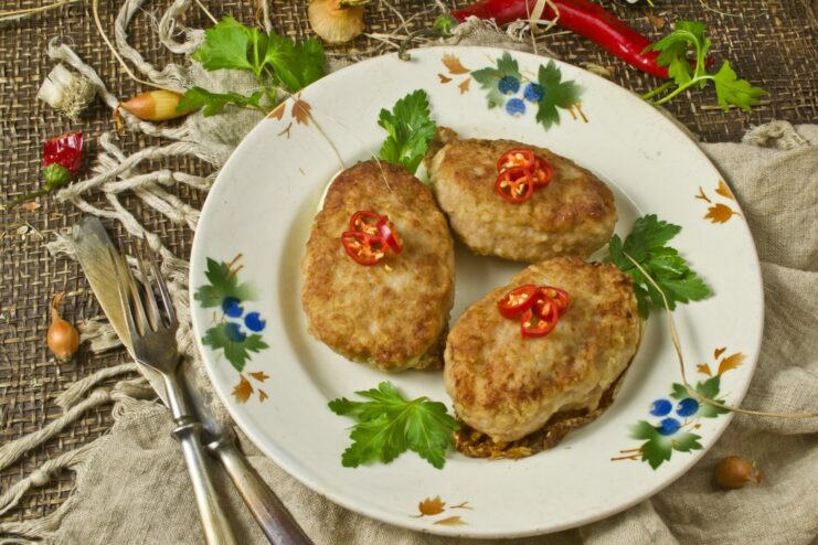 A plate of golden-brown, juicy pork patties with potatoes, garnished with fresh herbs.
