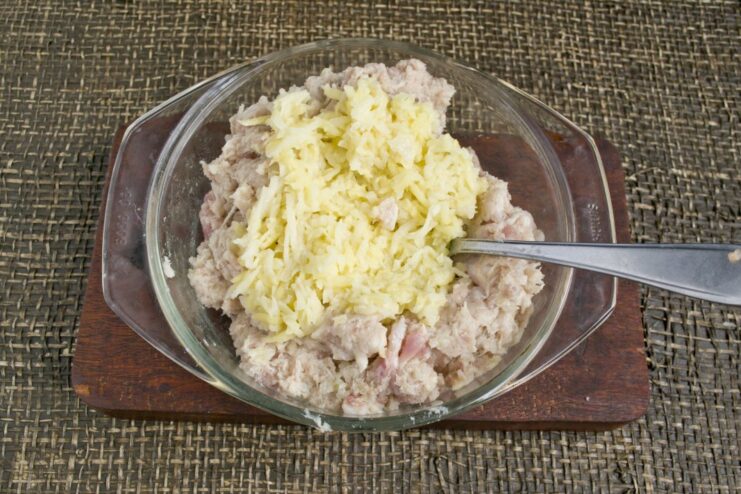 Grated raw potato being added to a bowl of fresh pork mince.