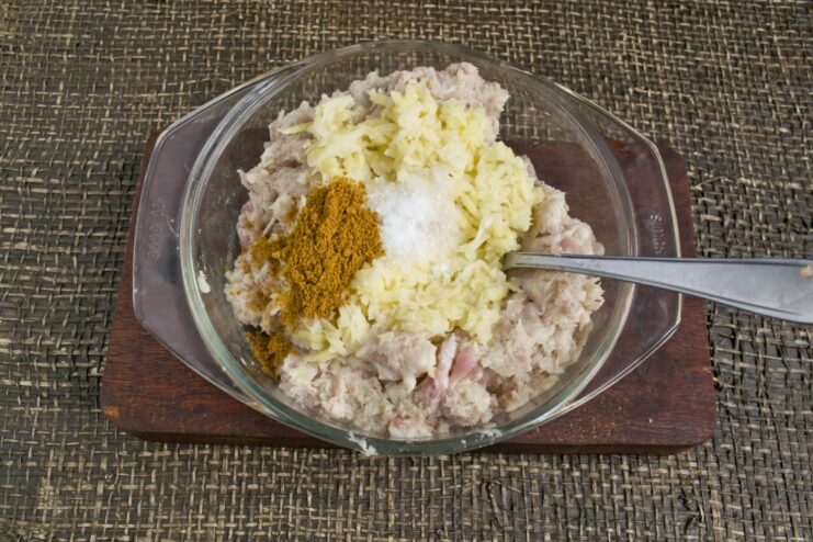 Adding salt and curry powder to the pork and potato mince in a bowl.