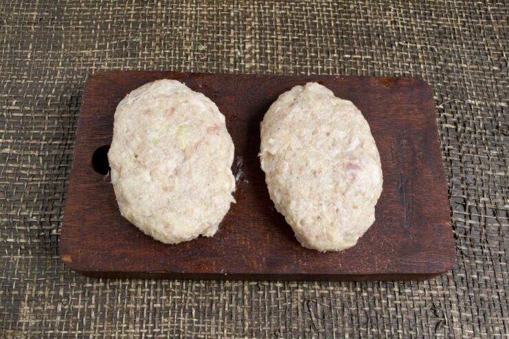 Hands shaping the raw pork mince mixture into oval patties.
