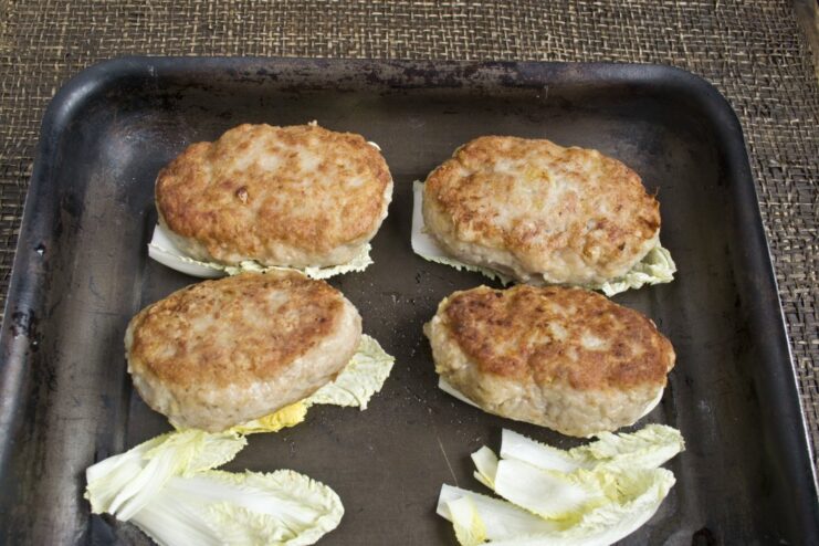 Golden-brown pork patties sizzling in a frying pan before being transferred to the oven.