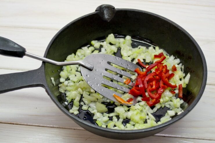 Adding a little heat with finely chopped chili pepper. Finely chopped red chili pepper being added to the sautéed onions in a skillet.
