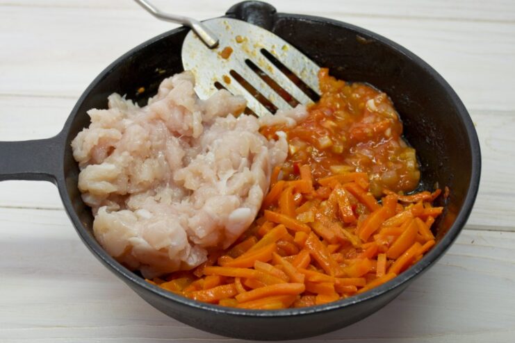 Cooking the ground chicken and carrots in the tomato base. Ground chicken and shredded carrots being mixed into the tomato sauce in the skillet.