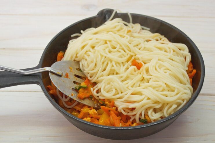 Tossing the cooked spaghetti with the rich, homemade sauce. Cooked spaghetti being tossed with the chicken and vegetable sauce in a large skillet.