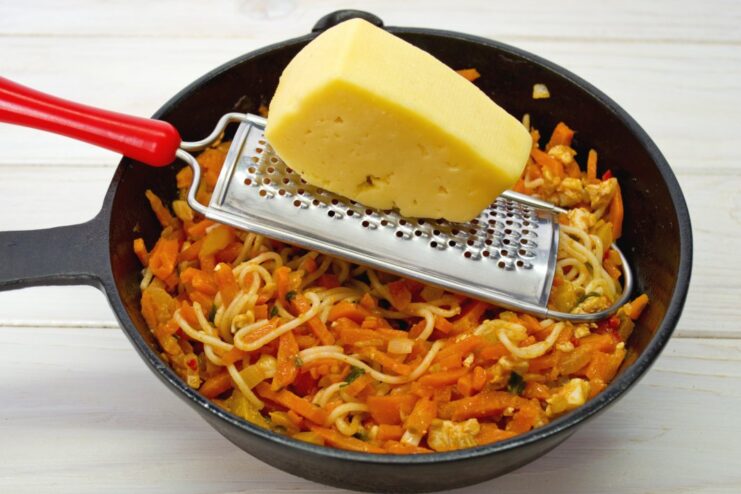 A generous sprinkle of grated cheese is the perfect finishing touch. A hand grating a block of hard cheese over the spaghetti.