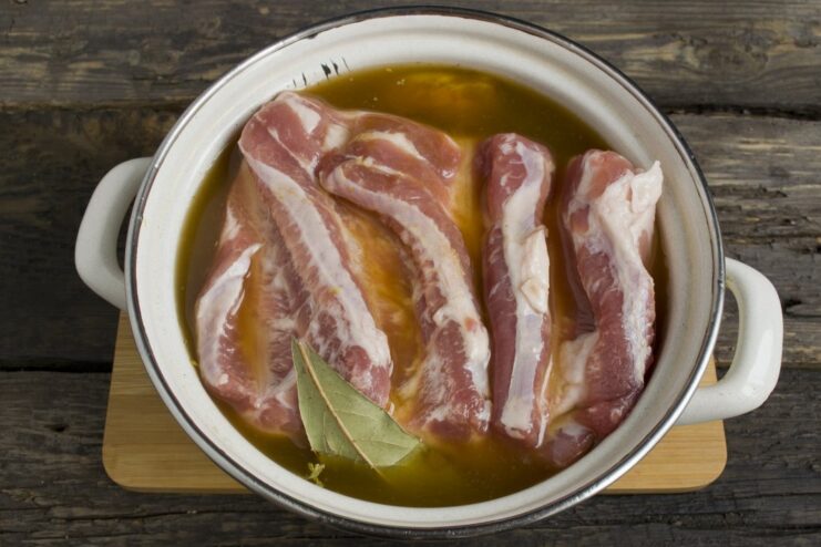 A pot with pork belly and vegetables being filled with beer, with salt and turmeric added.