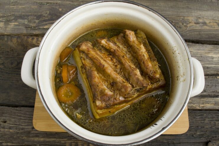 Cooked pork belly being removed from a pot, with a sieve ready to strain the broth.