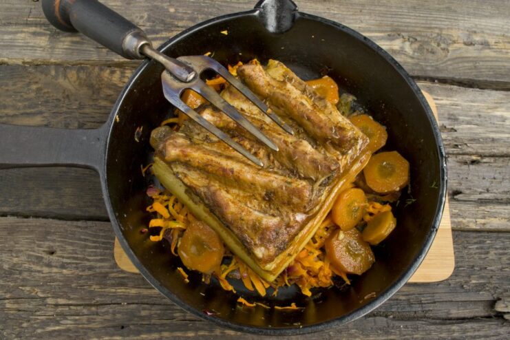 Boiled pork belly placed on a bed of sautéed carrots and onions in a skillet.