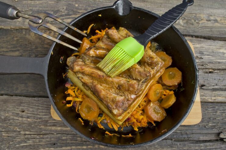 A hand brushing a dark balsamic glaze over the top of the cooked pork belly in a skillet.