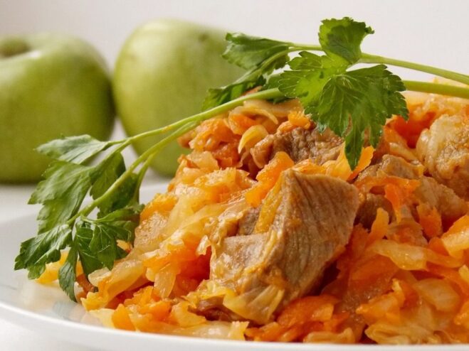 A plate of ready-to-eat braised cabbage with meat, garnished with fresh herbs.
