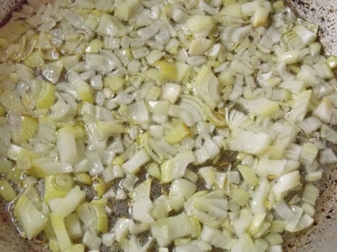 Sautéing onions until translucent to build the flavor base. Finely chopped onions being sautéed in a skillet with oil.