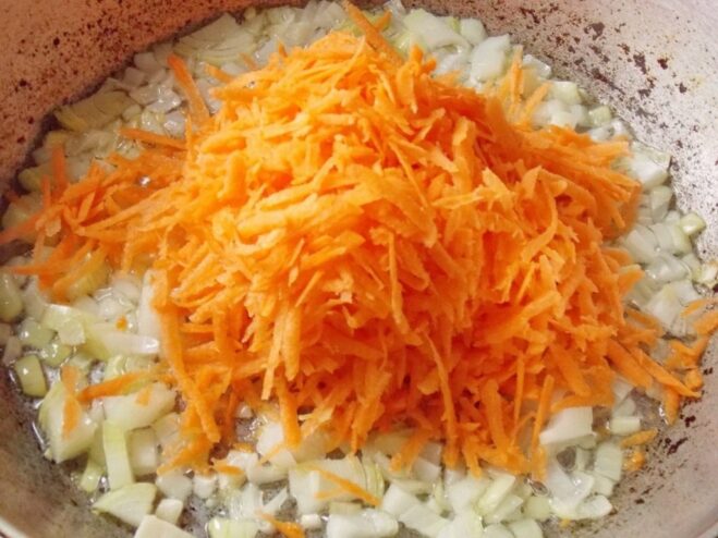 Adding grated carrots to the onions for a sweet and savory base. Grated carrots and chopped onions being fried together in a skillet.