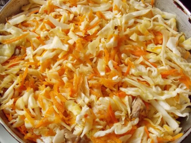 Mix everything well to combine the flavors before braising. Shredded cabbage being mixed with meat and vegetables in a large skillet.