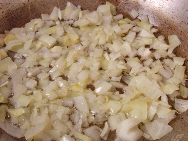 Sautéing Onions to Build Flavor Finely chopped onions being sautéed until translucent in a skillet.