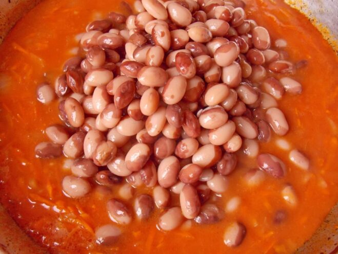 Combining Beans with the Flavorful Sauce Cooked beans being added to the tomato and vegetable sauce in the skillet.