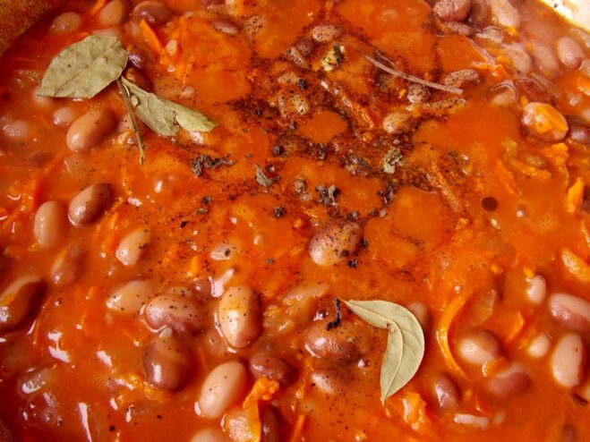 Seasoning the Stew with Aromatic Spices Spices, including a bay leaf and peppercorns, being added to the bean stew.