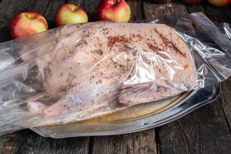 Using a Roasting Bag for a Juicier Duck A whole stuffed duck being placed inside a clear roasting bag.