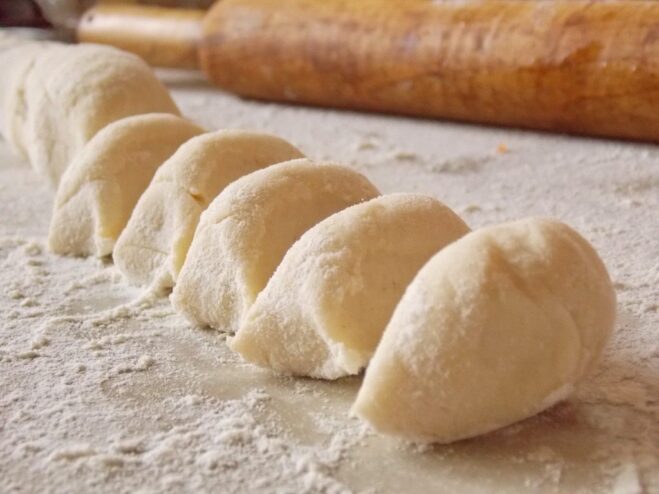 Shaping the dough into a log and cutting it into equal pieces. A log of dough on a floured surface being sliced into small pieces for vareniki.