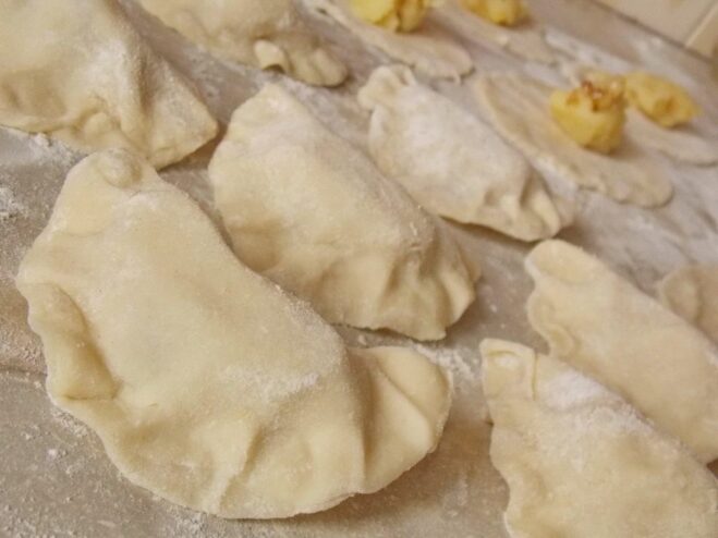 Pinching the edges of the vareniki to seal them securely. A hand carefully sealing a potato varenik, pinching the edges together.
