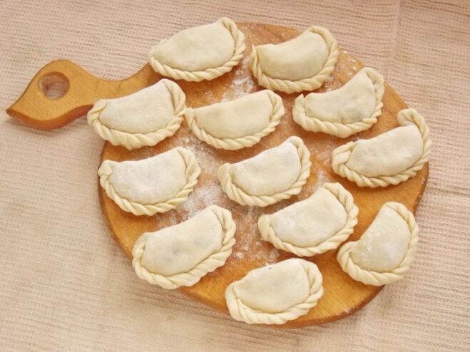 Arranging the uncooked vareniki on a floured board to prevent sticking. Rows of uncooked potato vareniki arranged on a floured wooden board.