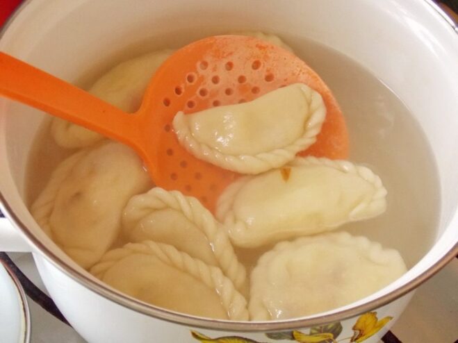 Dropping the vareniki into a pot of boiling water to cook. Potato vareniki being dropped into a pot of boiling salted water.