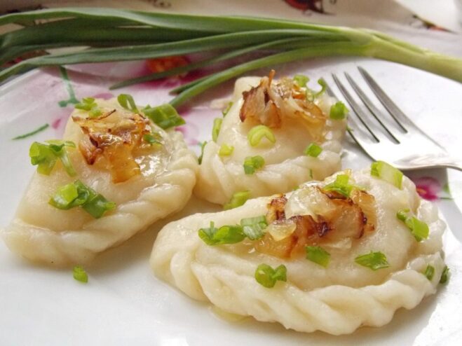 A perfect plate of homemade potato vareniki, ready to eat. A close-up shot of a plate of potato vareniki topped with fried onions and herbs.