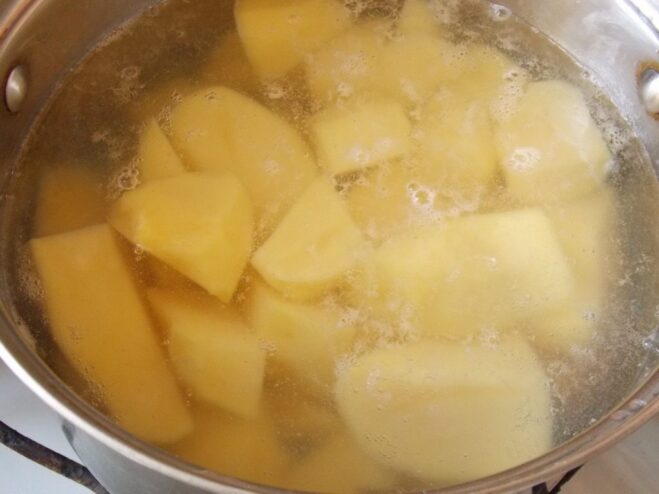 Boiling peeled and chopped potatoes until tender for the filling. Chopped potatoes boiling in a pot of water on the stove.