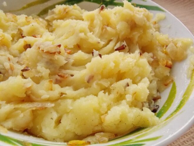 Combining the mashed potatoes and fried onions to finish the vareniki filling. The finished potato and onion filling for vareniki in a pot.