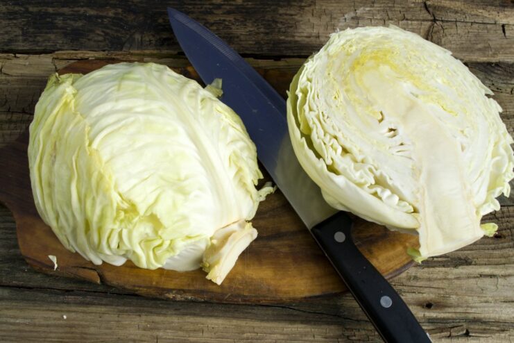 Step 1: Halving the Young Cabbage. The first step to preparing the schnitzel wedges. A head of young white cabbage being cut in half on a wooden cutting board.