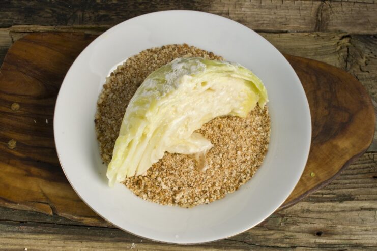 Final Breading Step: Breadcrumbs. Press gently to create a thick, even crust. An egg-washed cabbage wedge being thoroughly coated in a dish of breadcrumbs.
