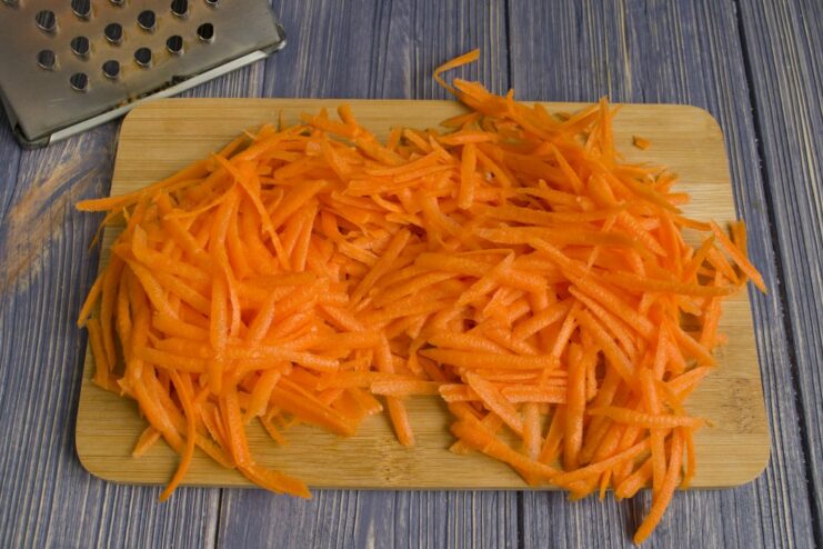 Step 2: Adding Grated Carrots to the Sautéed Onion Grated carrots being added to the skillet with sautéed onions.