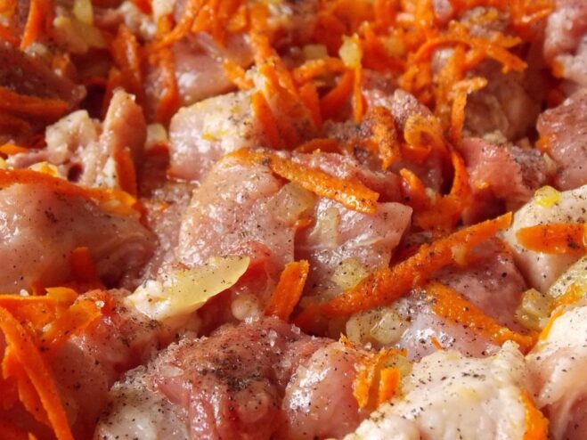 Browning pork pieces with vegetables for the stew Cubes of pork browning in a pan with sautéed onions and carrots.