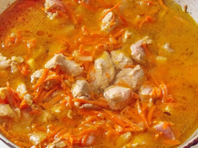 Simmering the pork stew base on the stove The meat and vegetable mixture simmering in a pan, covered with liquid.